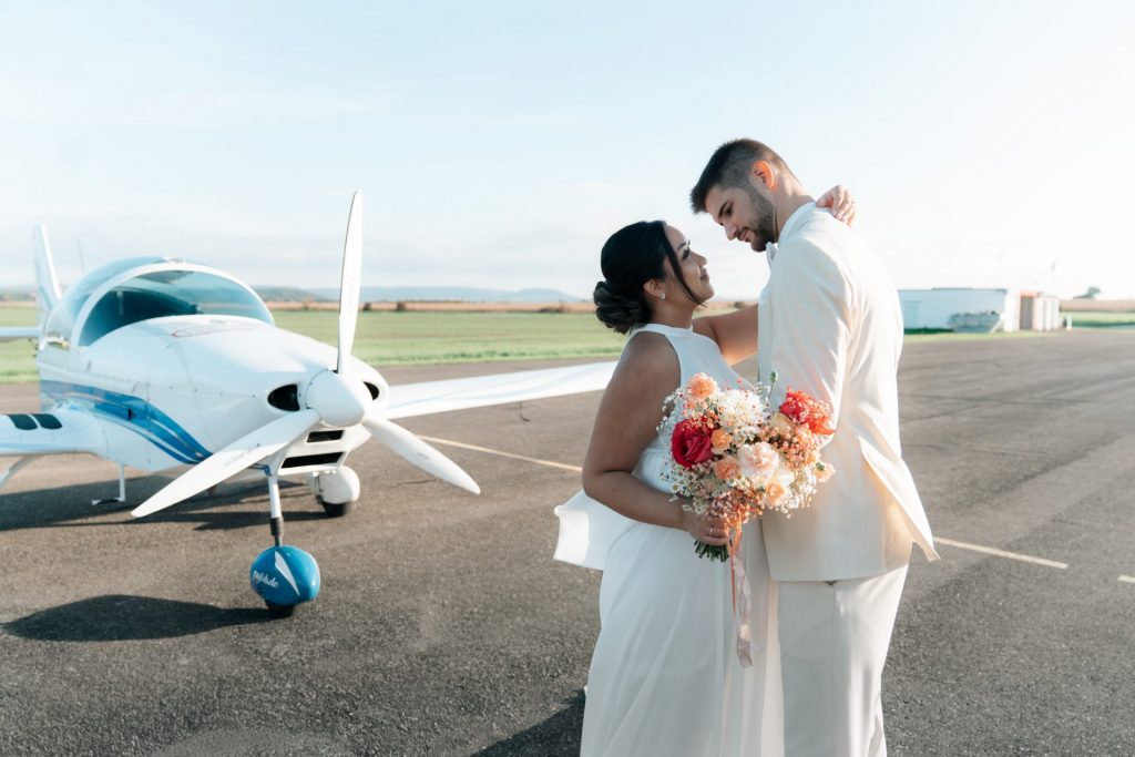 Brautpaar umarmt sich auf dem Flugplatz vor einem Kleinflugzeug – emotionale Hochzeitsfotografie in Donaueschingen